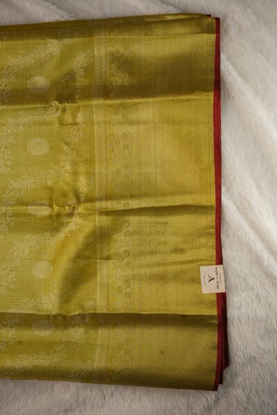 Close-up texture of a golden yellow pure tissue Kanjeevaram Pattu saree revealing woven checks, large floral wreath motifs, and a detailed zari border with a red edge.