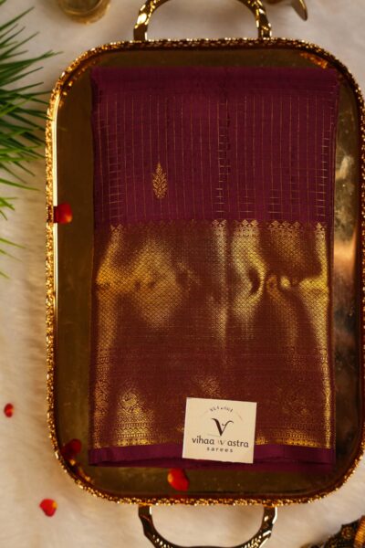 Top view of the beautifully folded self maroon pure handloom Kanjeevaram Pattu saree resting on a decorative brass tray, showcasing the delicate gold checks and heavy border.