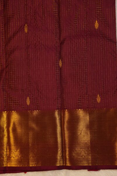 Close-up texture of the pure handloom maroon silk body showing the woven vintage gold zari checks (kattam) with enclosed buttis, alongside the heavy, intricate gold work of the Kanchi border.