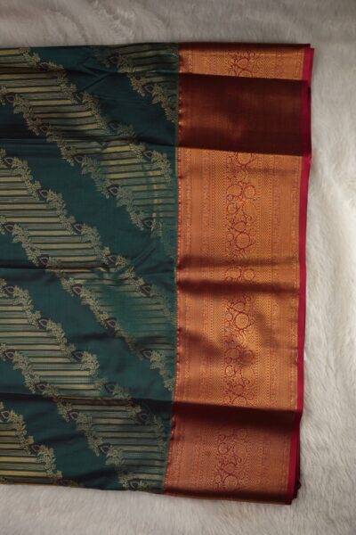 Close-up texture of the sea green blended silk body showing woven gold buttis alongside the heavy, intricate gold zari peacock work of the pink Kanchi border.