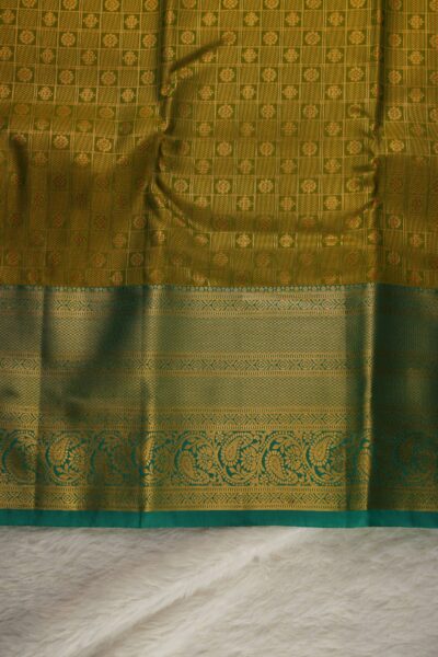 Close-up texture of the mustard yellow blended silk body showing the classic gold zari checks (kattam) alongside the heavy, intricate gold zari work of the sea green Kanchi border.