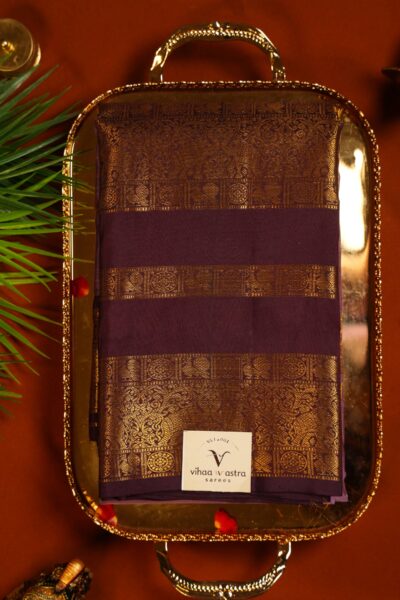 Folded light burgundy pure handloom Kanjeevaram saree on a brass tray, highlighting the rich dark maroon multi-band Kanchi gap border woven with gold zari peacocks.