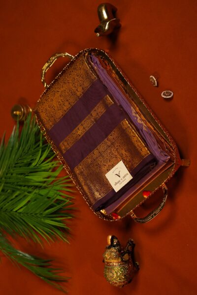 Angled top view of the beautifully folded light burgundy handloom Kanjeevaram silk saree resting on a decorative tray alongside traditional Indian decor elements.