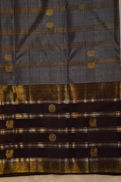 Close-up texture of the pure handloom elephant grey silk body showing woven vintage gold zari lines alongside the heavy, intricate gold zari work of the brown Kanchi border.