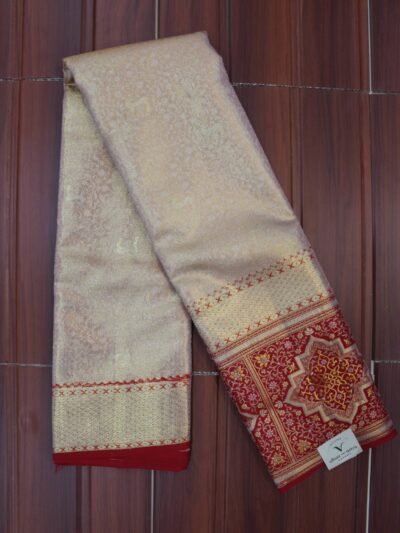 Folded majestic champagne gold pure Kanjeevaram tissue silk saree with subtle woven motifs, showcasing a rich contrasting red border and heavy gold zari pallu with highly intricate geometric and floral patterns.