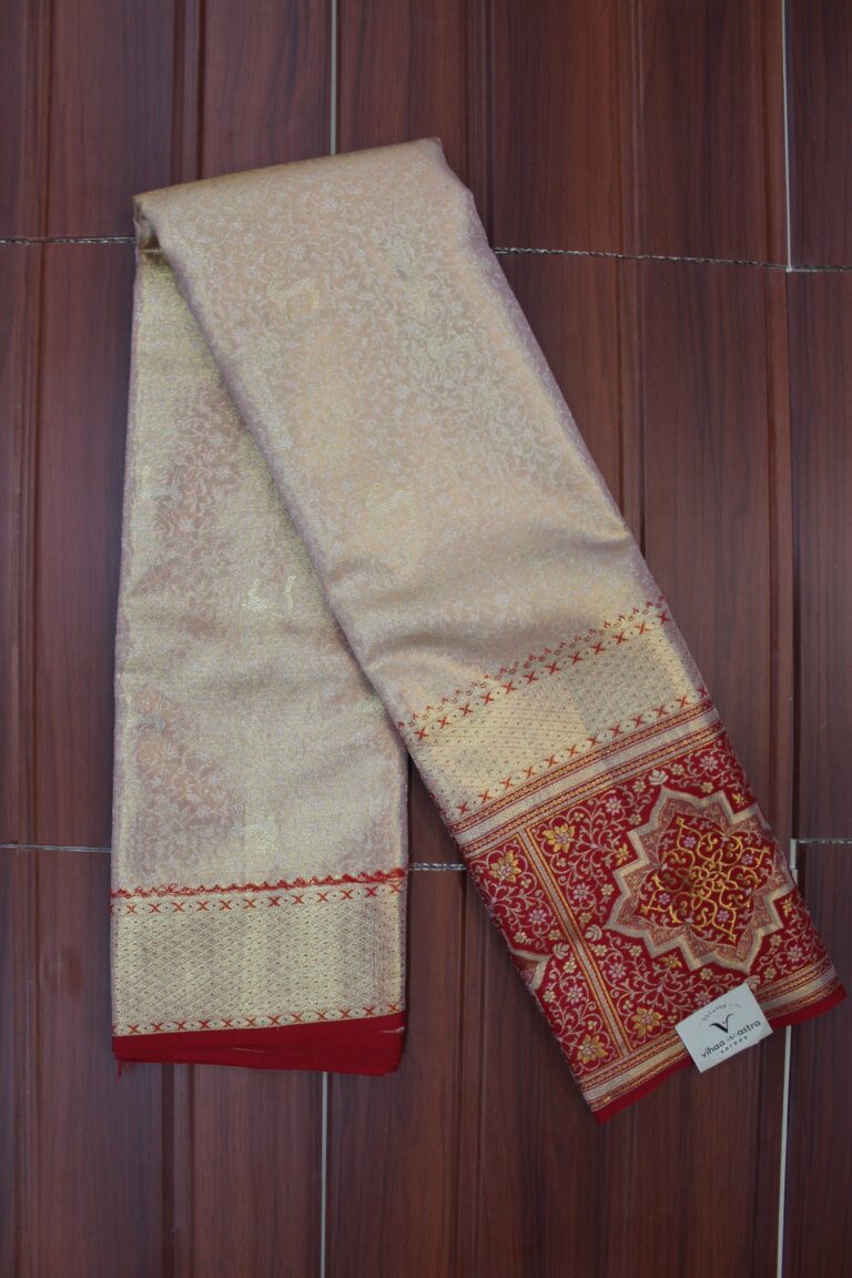 Folded majestic champagne gold pure Kanjeevaram tissue silk saree with subtle woven motifs, showcasing a rich contrasting red border and heavy gold zari pallu with highly intricate geometric and floral patterns.