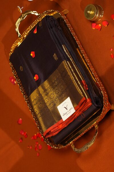 Folded deep coffee brown pure handloom Kanjeevaram saree on a decorative tray, highlighting gold zari bird motifs and a rich border with a red Korvai edge.