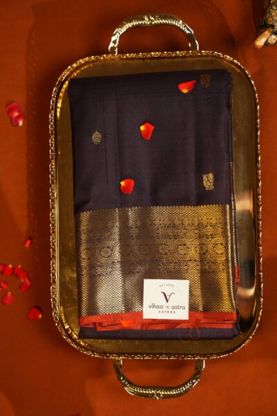 Top view of the neatly folded coffee brown pure handloom Kanjeevaram saree resting on a brass tray amidst scattered rose petals.