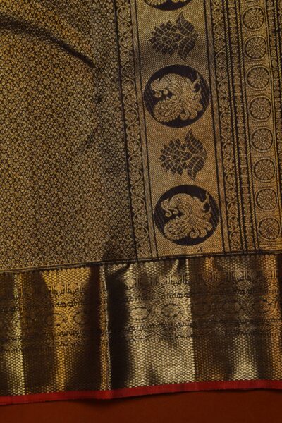 Close-up detail of the heavy gold zari border on the coffee brown Kanjeevaram saree, revealing intricate peacock roundels and diamond brocade next to the red edge.